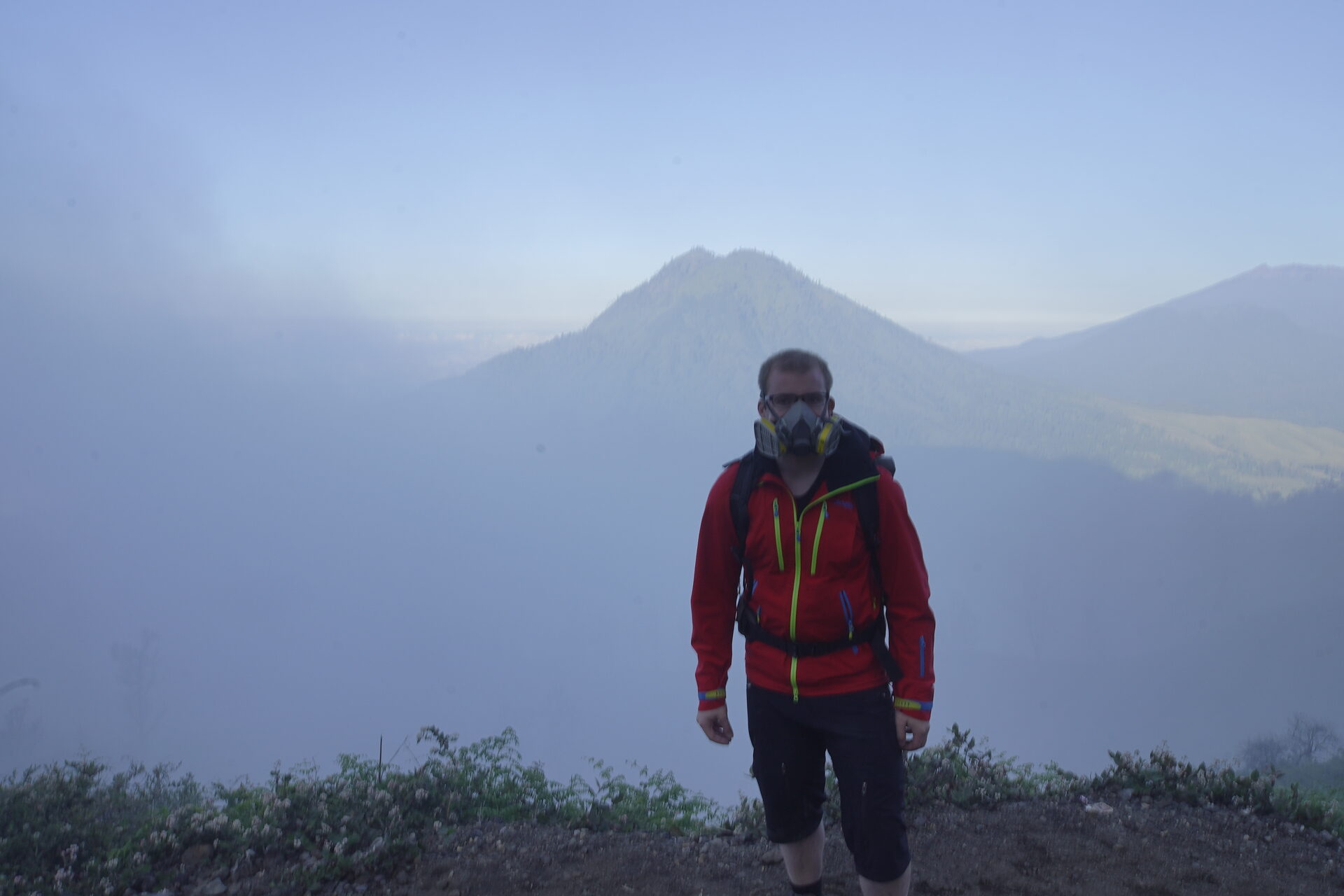 Trekker mit Gasmaske vor Vulkanpanorama